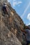 Girl climbing a rock wall looking for the best grip laterally while her partner belays her from below