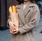 A girl in a coat and hat holds a bag with baguettes, bread, a loaf, on the street. a shopping trip, morning.