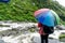 Girl with colorful umbrella looking out over a flowing river with plant covered hills behind it