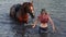 Girl comes out of a lake in clothes with her horse