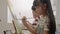 A girl concentrates on acrylic color painting on canvas in an art classroom.