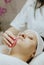 A girl cosmetologist cleanses the patient s face with a scrubbing sponge.