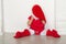 Girl in costume of Santa closes face sitting on floor