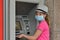 A girl counts money in a protective mask during a covid quarantine near an ATM