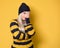 Girl covering face with hand. Shame, model wearing woolen cap and sweater, isolated on yellow background. Ashamed young woman