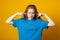 Girl covering her ears with hands for not to hear anything. Photo of young girl dressed in casual clothes on yellow background