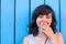 Girl covers her mouth with her hand, on the background of blue wooden walls.