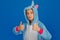 A girl in a cozy blue unicorn costume poses in the studio on a blue isolated background. Shows thumbs up. Place for text