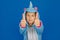 A girl in a cozy blue unicorn costume poses in the studio on a blue isolated background. Shows thumbs up. Place for text
