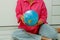 a girl in a crimson shirt and jeans sitting on the floor holds a globe in her hands