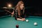A girl with a cue in her hands makes a shot at a ball in a billiard club.Russian billiards