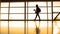 The girl with cup of coffee going in airport in front window opposite the runway, silhouette, warm