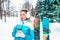 A girl with cup tea coffee, in white warm ears, is standing in a winter park against background of Christmas trees and