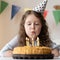 A girl with a cute face blows out candles on her birthday birthday cake. He is standing on the table at which the child