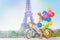 Girl cycling through Paris with colorful balloons