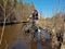 Girl cyclist overcomes wading deep puddles on clay forest road in spring