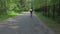 Girl cyclist rides along asphalt road past green trees