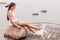 A girl dangles her bare feet in the water while sitting on a large stone.