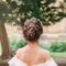 Girl with dark hair and delicate skin shows gorgeous hairstyle from large number of braids, lady stands with her back to