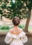 Girl with dark hair and delicate skin shows gorgeous hairstyle from large number of braids, lady stands with her back to