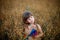 A girl with dark hair sits in a field that looks like wheat