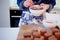 Girl decorates cupcakes, holding plate, muffins and plate of ingredients for decoration on the table.