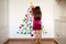 Girl decorates the wall with multicolored circles forming a Christmas tree