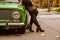 A girl in a denim jacket and black stockings, pantyhose and a black skirt is leaning over the green retro car. Legs closeup