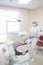 Girl dentist, in white clothes, mask and cap stands next to a modern dental chair in a large, simple, medical office