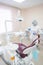 Girl dentist, in white clothes, mask and cap stands next to a modern dental chair in a large, simple, medical office