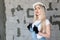 Girl designer foreman blonde in construction helmet, textile black protective gloves, denim overalls standing near gray wall Cibit
