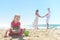 Girl digging sand on beach with parents in background