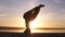 The girl does asana in yoga, slowly raises her legs in the rack on her head. Silhouette of a woman in the background of