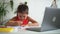 Girl doing homework and smiling while sitting at table with laptop while studying at home spbd.