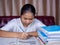 Girl doing homework on a wooden table and there was a pile of books next to it The background is a red sofa and cream curtains