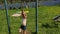 The girl is doing sports on the street on a warm summer day. The child performs exercises on the rings.