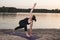 Girl Doing Yoga on a mat on the beach by the river at sunset, twisting in a standing position. Extended Side Angle Pose