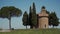 Girl in dress  goes from large green tree to old stone chapel Cappella Vitaleta