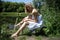 A girl in a dress on the shore of a lake sits on an old bench on a Sunny day.