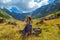 Girl in dress and straw hat sits on a rock against of high mountains