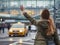 Girl dressed autumn outfit calling yellow taxi cab raising arm waving gesture in the city airport arrival zone. Traveling, airport