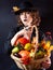 A girl dressed in black on a black background with a basket of vegetables. Autumn leaves. Halloween Costume