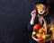 A girl dressed in black on a black background with a basket of vegetables. Maple leaf in the hands of a girl. Halloween costume
