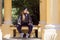 A girl dressed in hip-hop style sits on a bench between the columns in the park. Modern girl in classical architecture