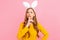 Girl in the ears of an Easter Bunny, holding her front finger over her lips, making a gesture of silence, on an pink background