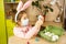 A girl in the ears of a hare makes an Easter bunny in a medical mask out of an egg and plasticine. DIY sitting at home, preparing