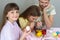 A girl with an egg in her hands looked into the frame, in the background the family paints eggs in glasses with dyes