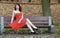 Girl in elegant red dress sitting on bench in autumnal park