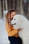 Girl embracing cute big white dog in winter park. The girl with the Maremma . Forest on background
