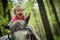 Girl enjoying horseback riding in the woods, young pretty girl with blond curly hair on a horse with backlit leaves